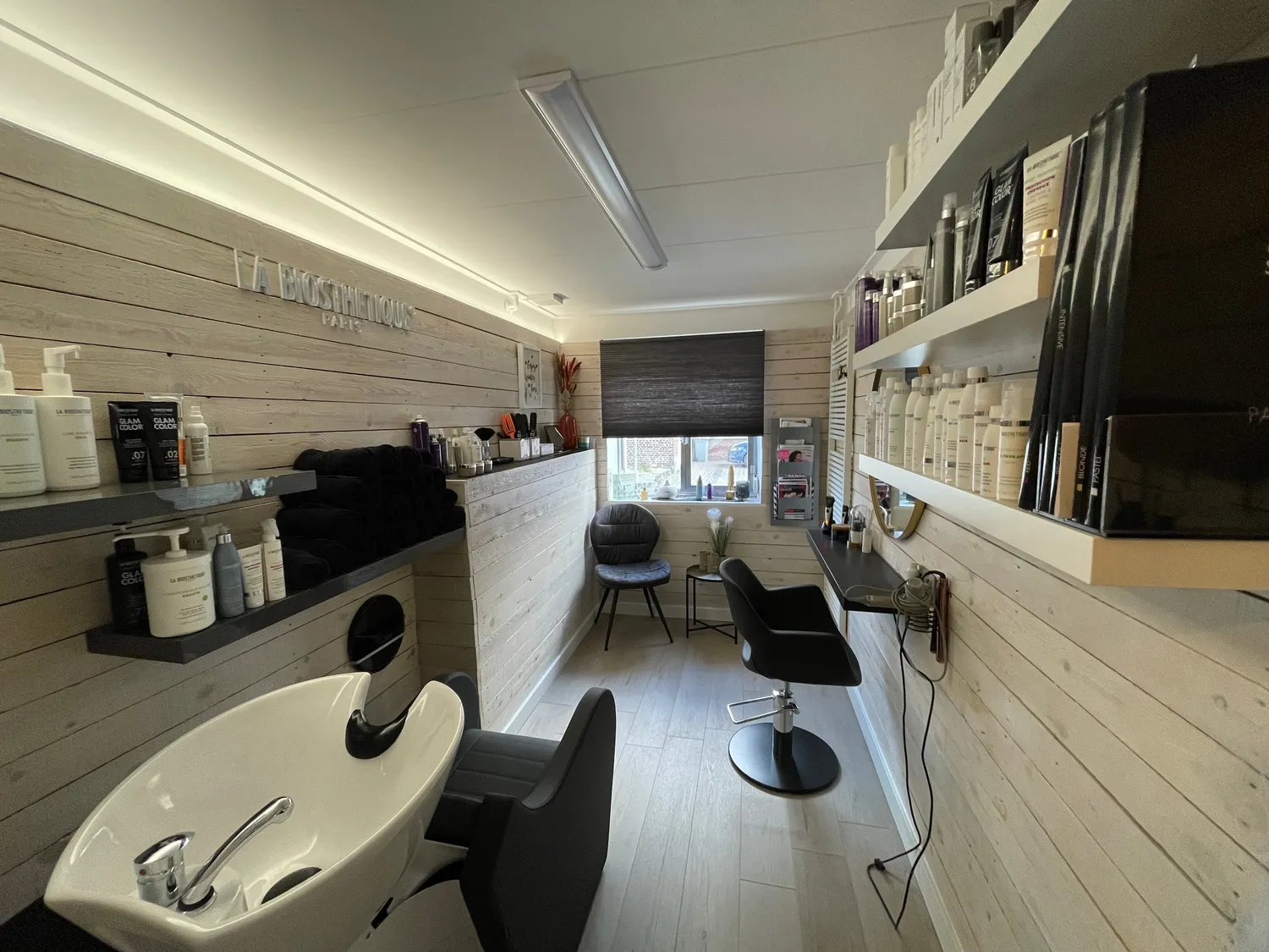 Overzicht van de salon met lichte houten wanden, wasstoel en werkplek